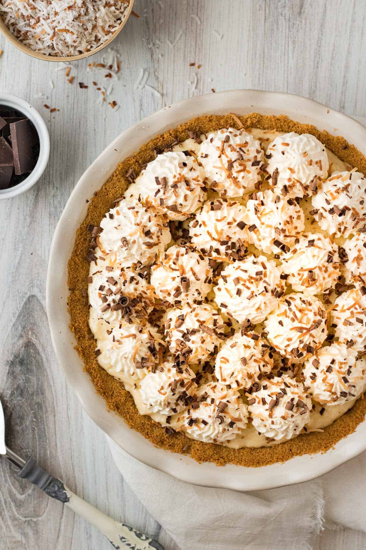 chocolate coconut cream pie in white pie dish with whipped cream and toasted coconut on top