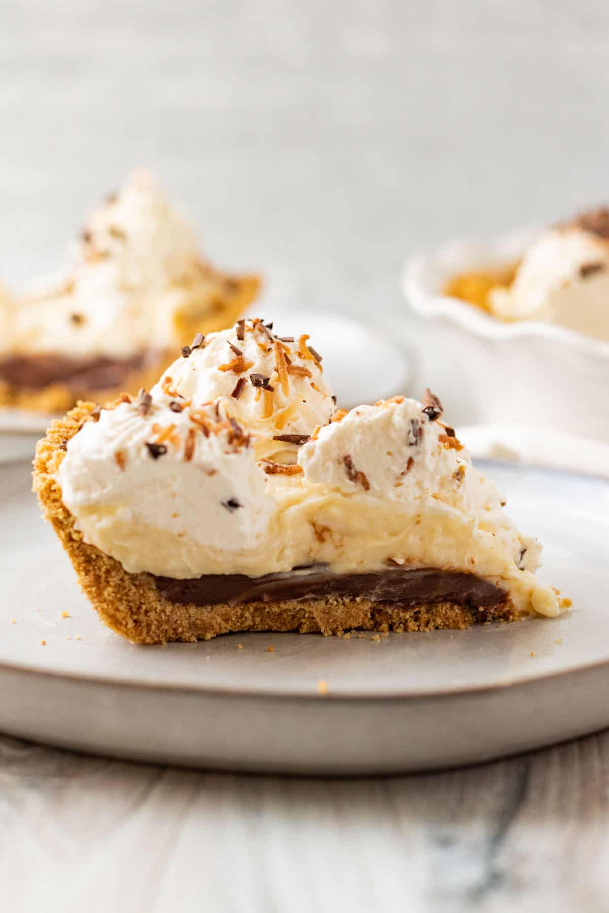 slice of chocolate coconut cream pie with whipped cream on a gray plate with another slice in background