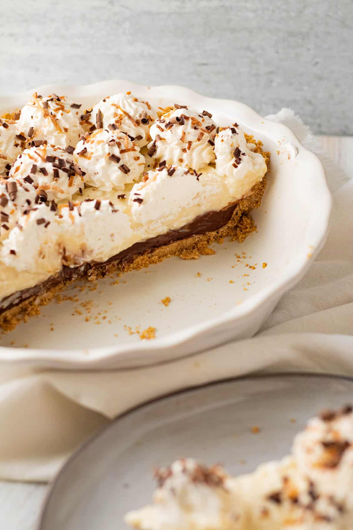 white pie dish with chocolate coconut cream pie filling half of dish and slice of pie on a plate in front