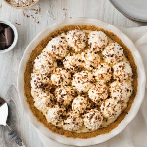 chocolate coconut cream pie in white pie dish with whipped cream and toasted coconut on top