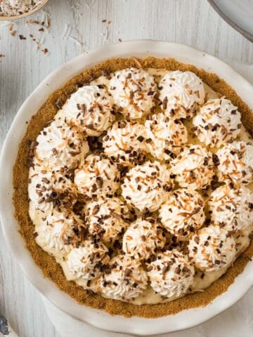 chocolate coconut cream pie in white pie dish with whipped cream and toasted coconut on top