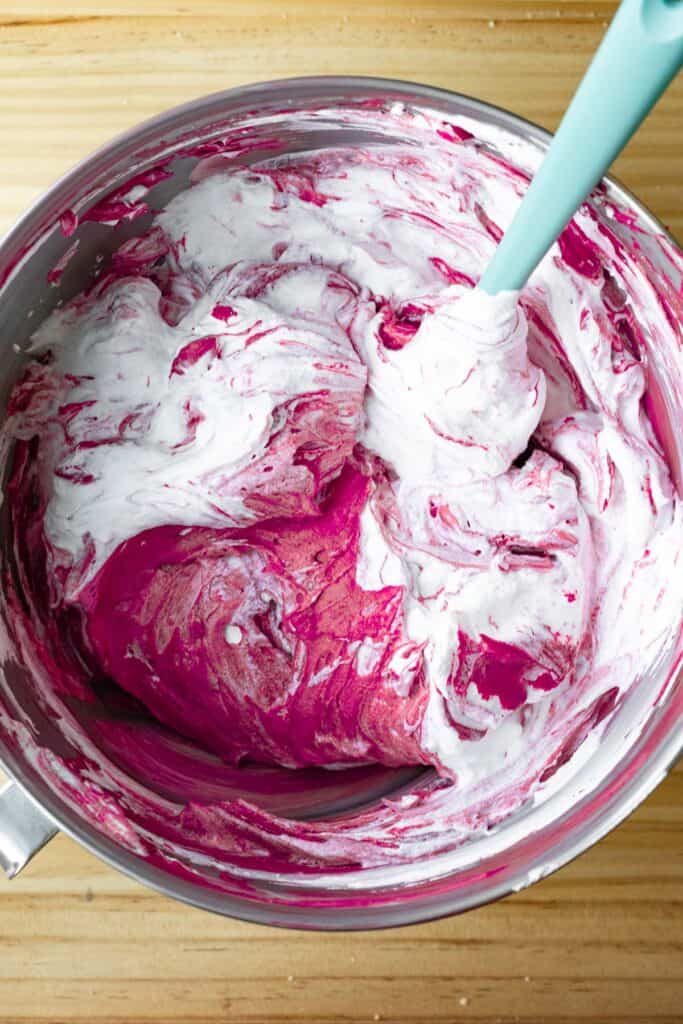 mixing bowl with red velvet cheesecake filling being folded with whipped cream