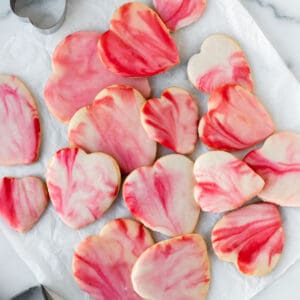 pile of red and pink marbled heart shaped sugar cookies on white parchment paper