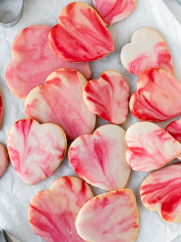 pile of red and pink marbled heart shaped sugar cookies on white parchment paper