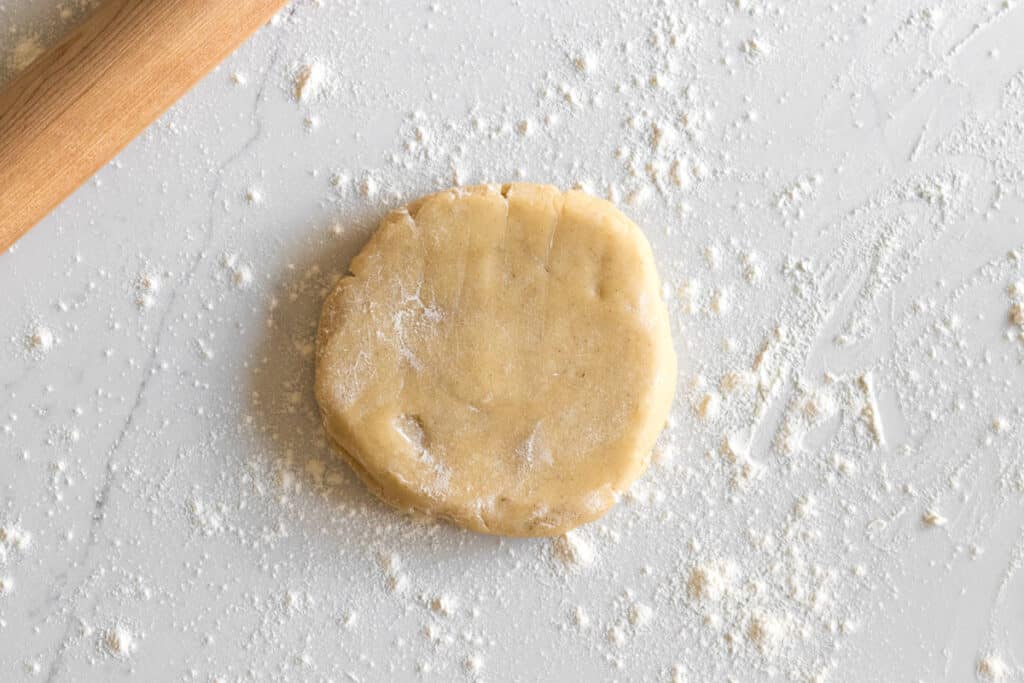 disc of sugar cookie dough with wood rolling pin