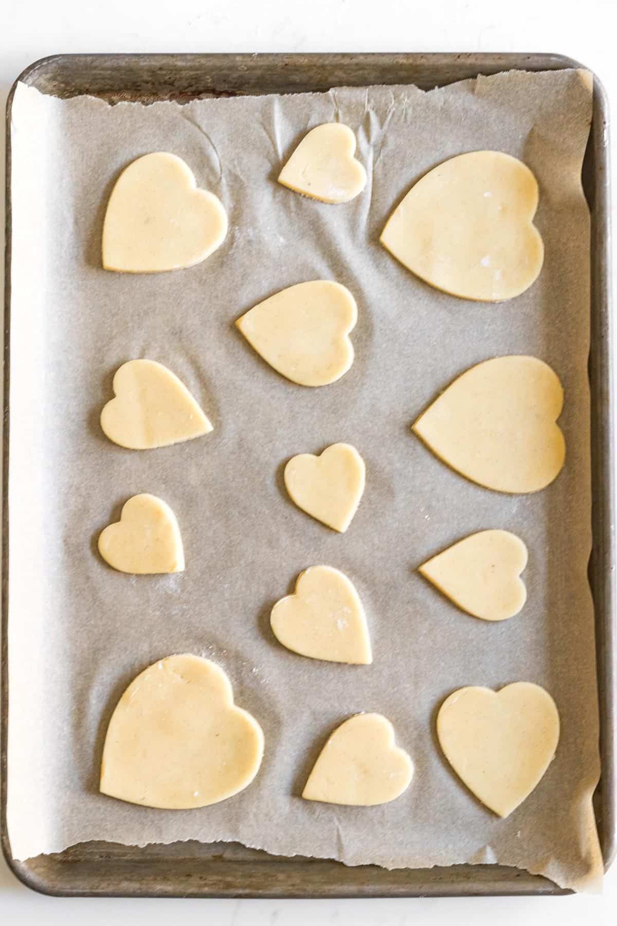 sheet tray line with parchment paper with different sized heart cut out sugar cookies
