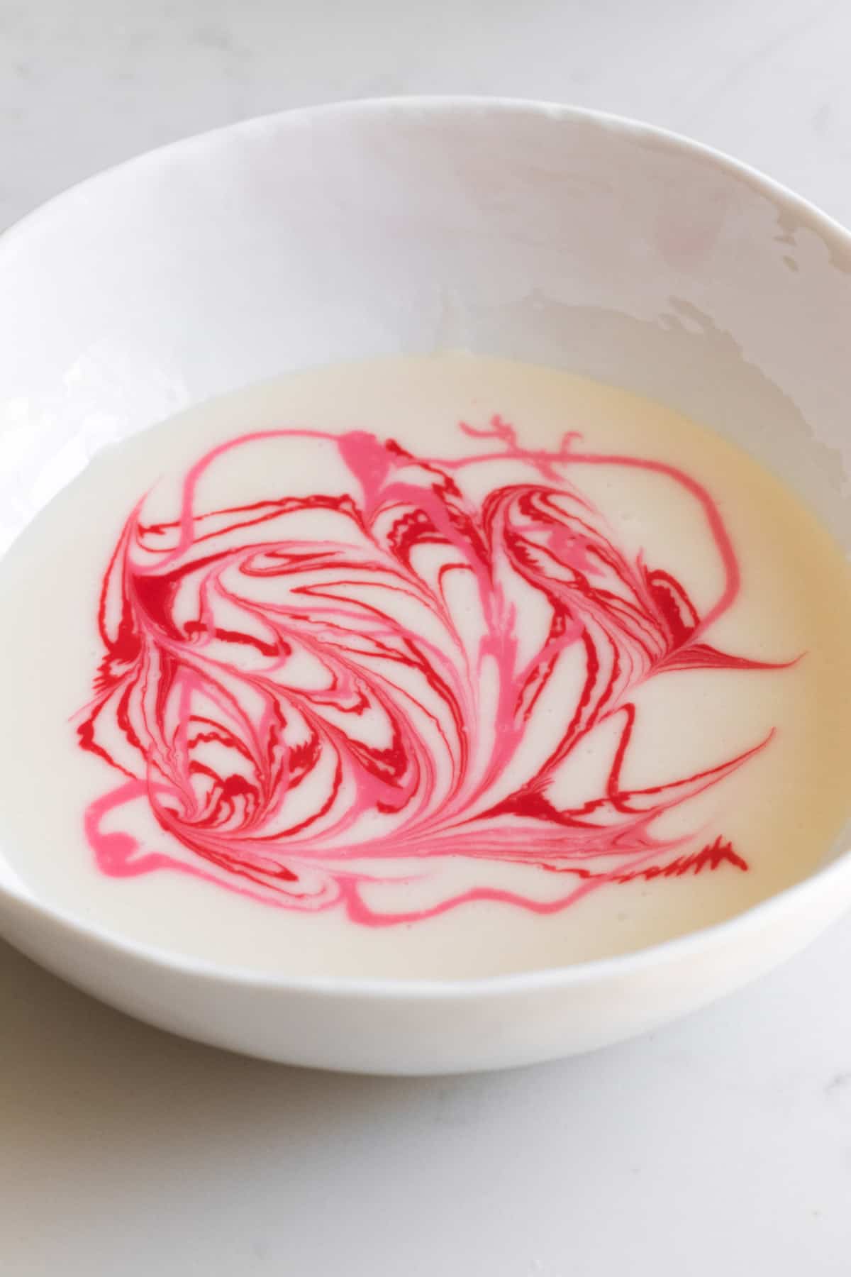 bowl of white icing with pink and red swirls in it