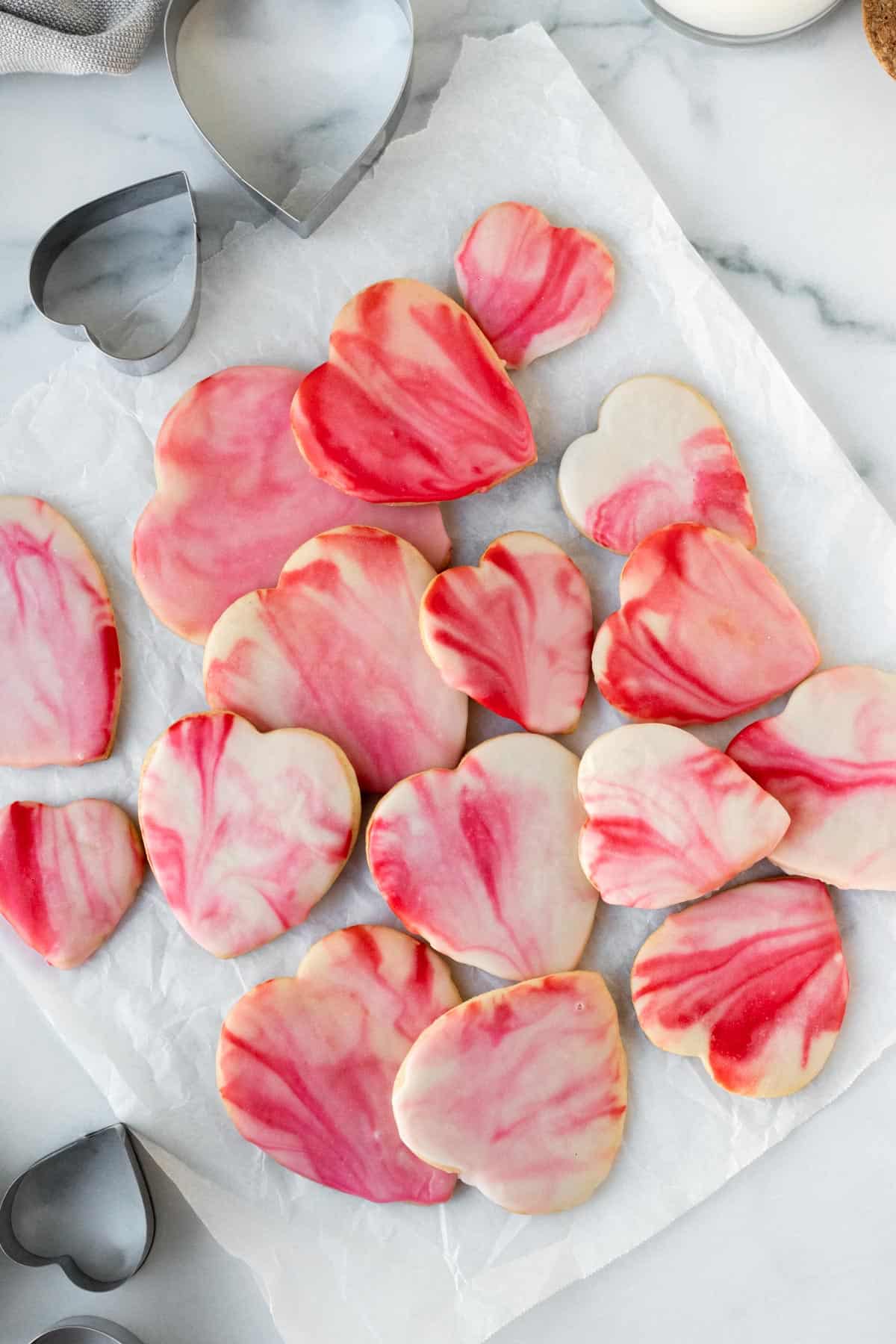 pile of red and pink marbled heart shaped sugar cookies on white parchment paper