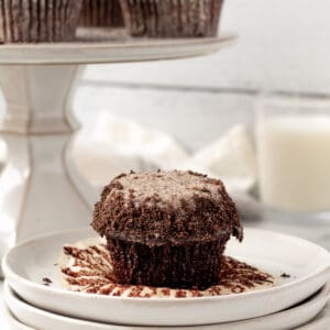 chocolate cupcake with oreo buttercream sitting on a stack of plates with glass of milk in background