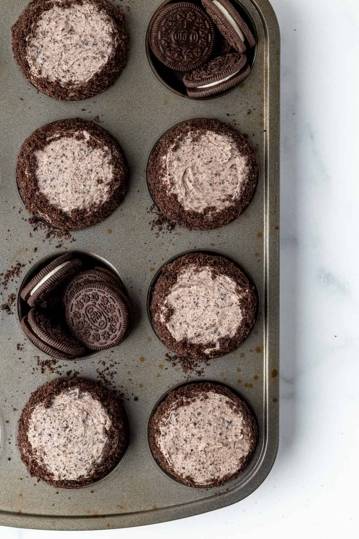 oreo cupcakes in cupcake tin with 2 tins filled with oreo cookies