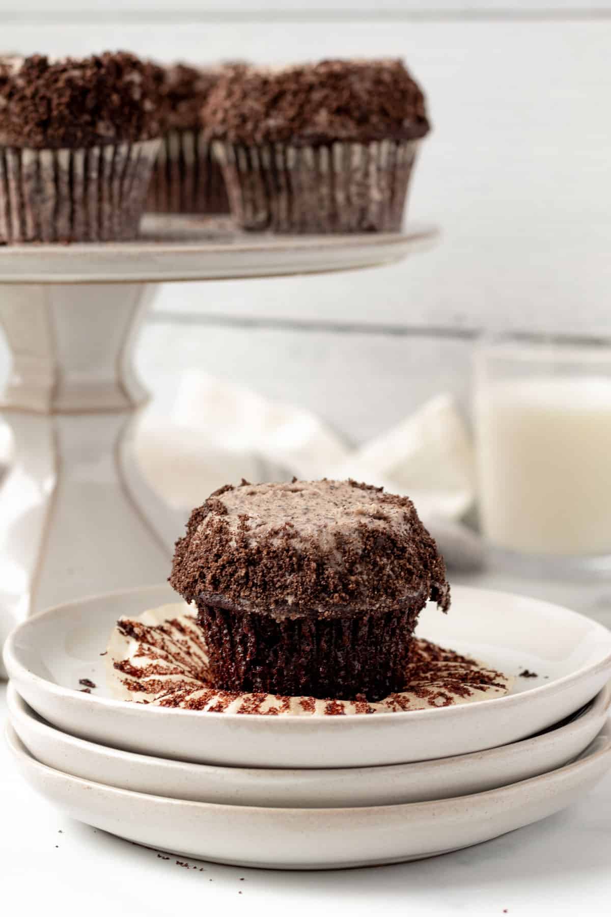 chocolate cupcake with oreo buttercream sitting on a stack of plates with glass of milk in background