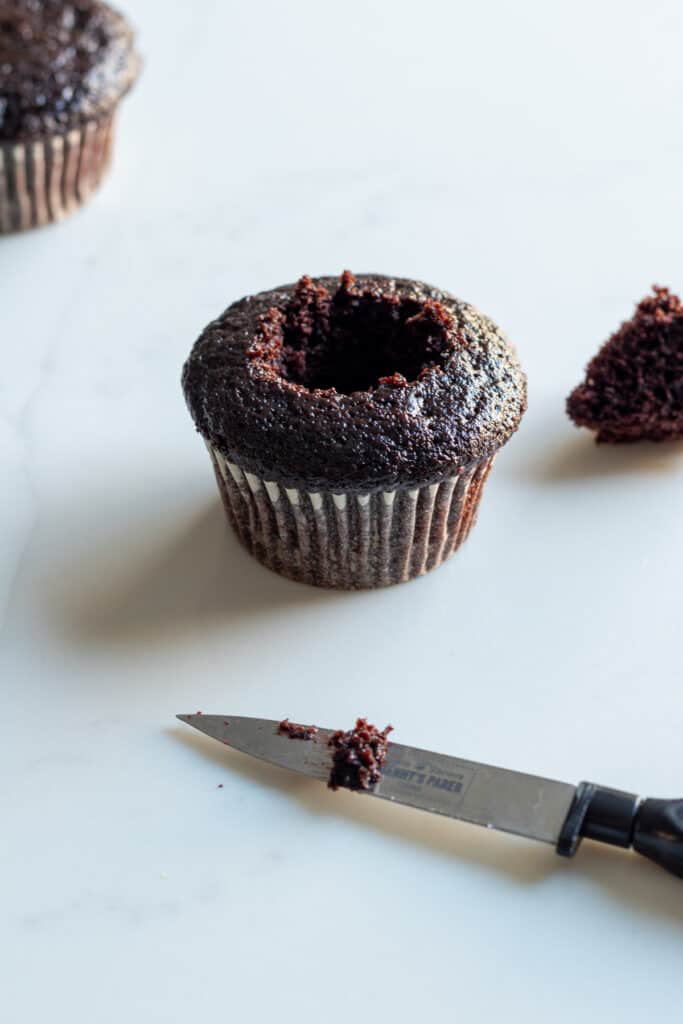 chocolate cupcake with middle cut out of it and knife in front of cupcake