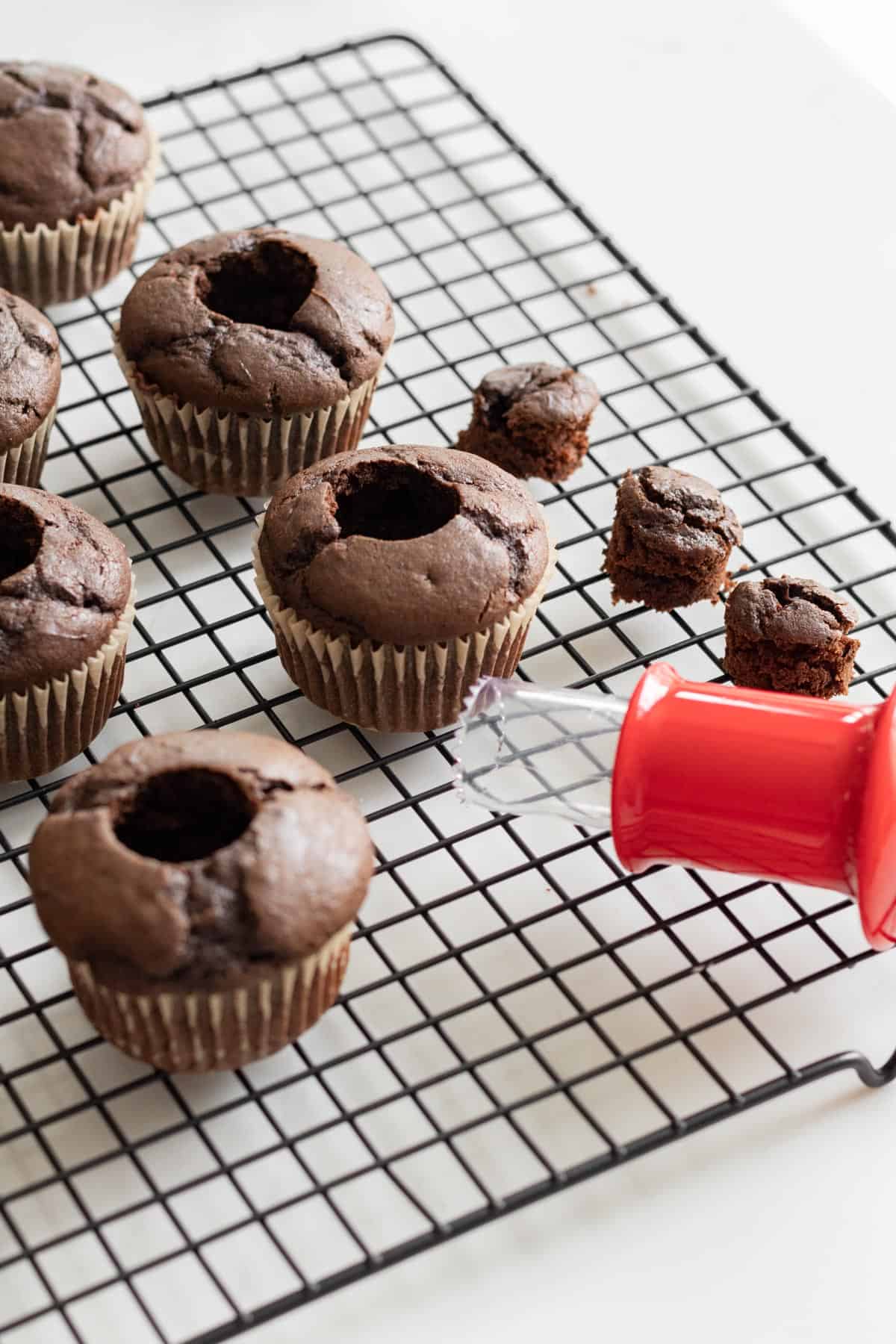 chocolate cupcakes with middles cut out sitting on a cooling rack with cupcake corer 