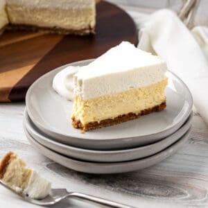 slice of vanilla bean cheesecake on stack of plates with bite of cheesecake on a fork in front of cake