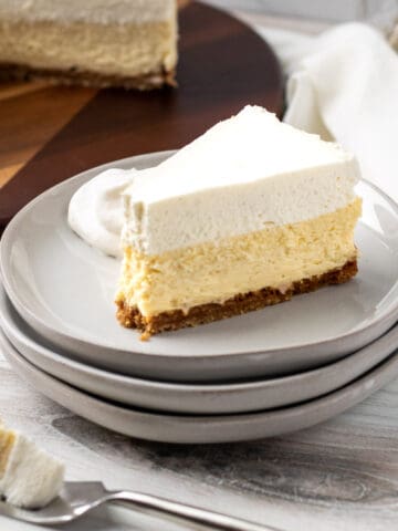 slice of vanilla bean cheesecake on stack of plates with bite of cheesecake on a fork in front of cake