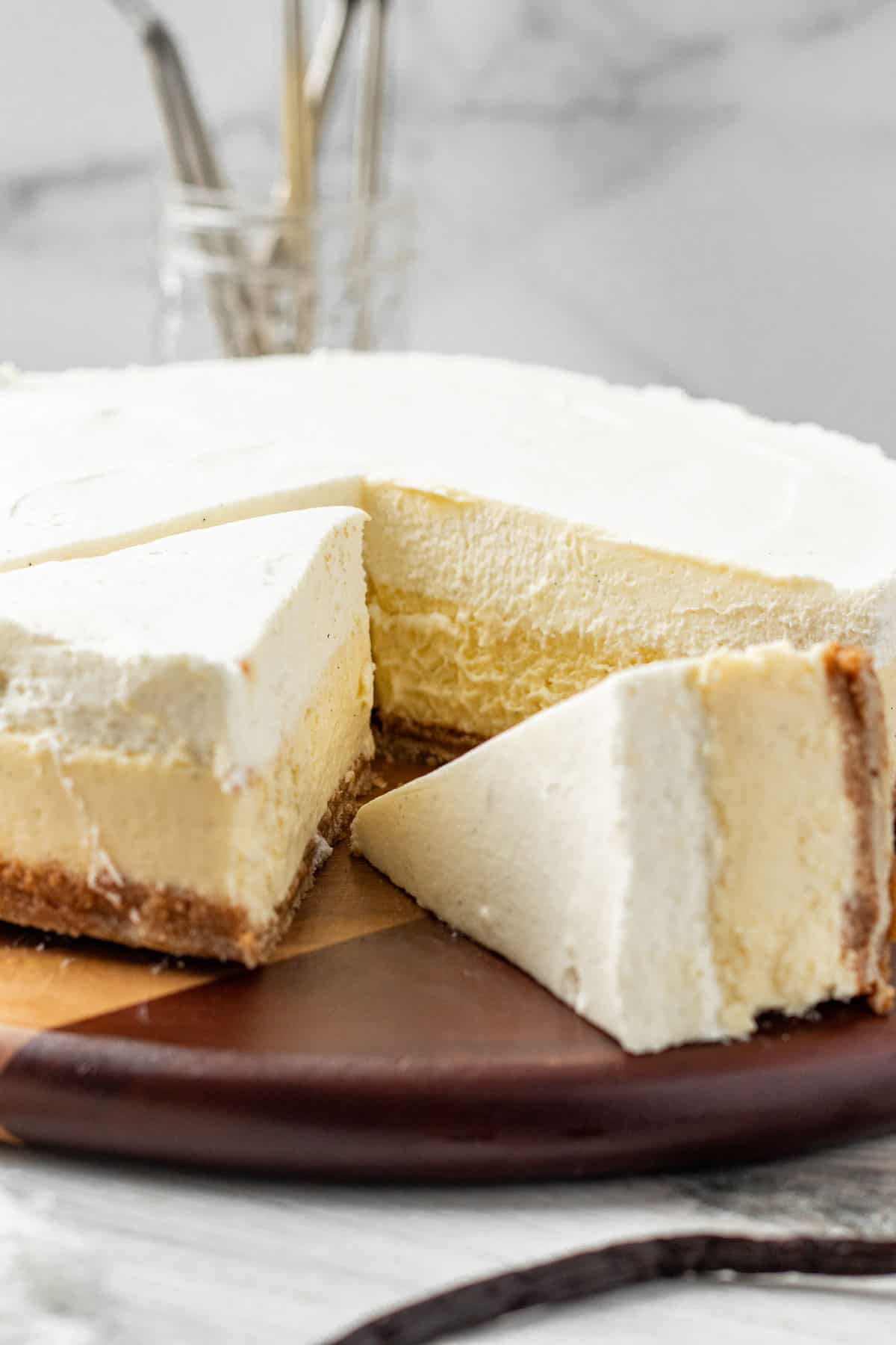 cheesecake sitting on wooden board with one slice cut and another slice cut and laying on its sides showing layers