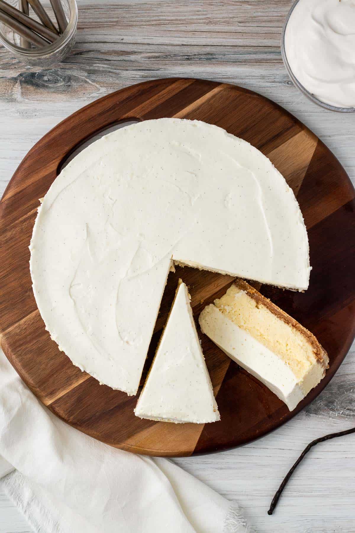 overhead view of a vanilla bean cheesecake with 2 slices cut out sitting on a round wooden board