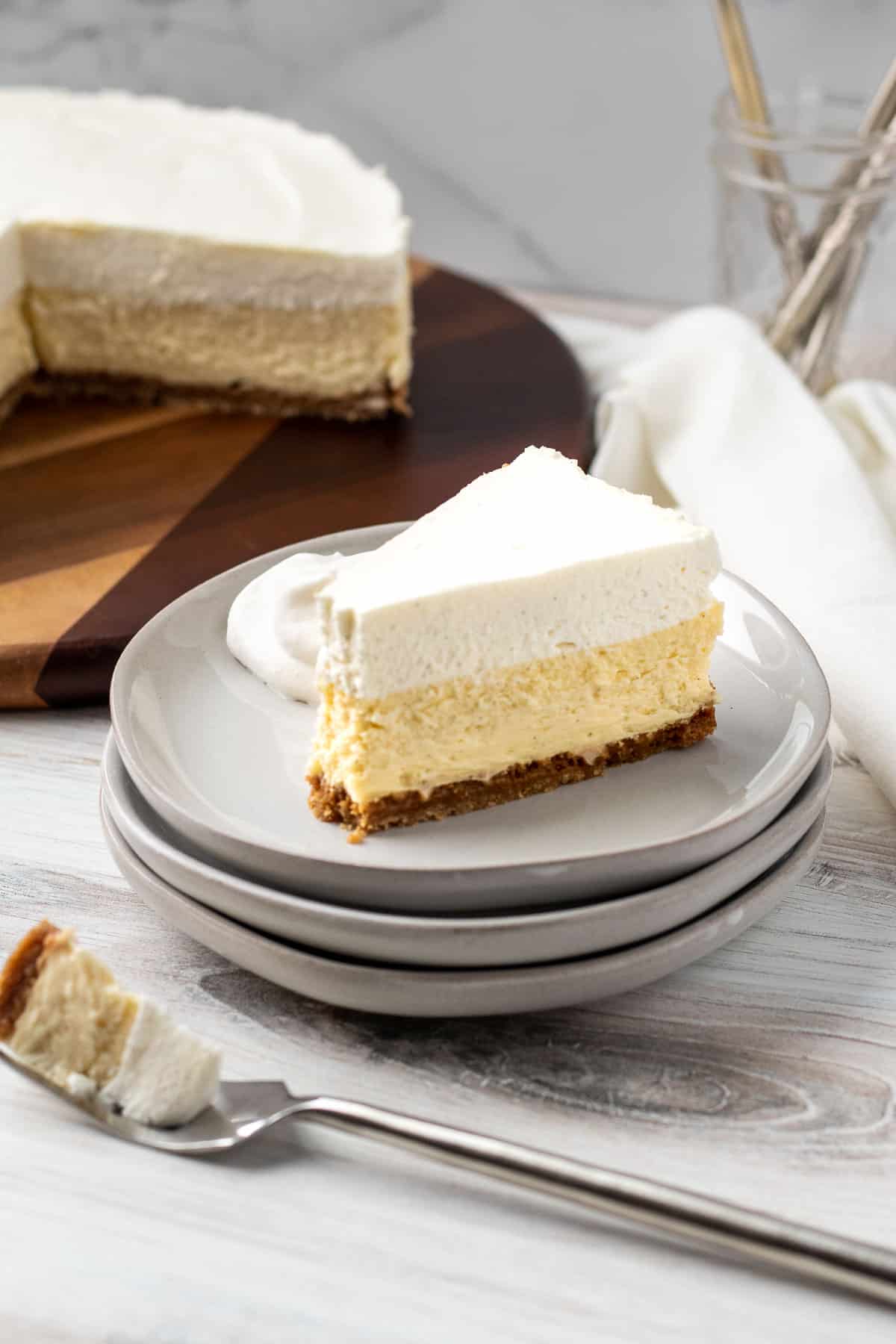 slice of vanilla bean cheesecake on stack of plates with bite of cheesecake on a fork in front of cake