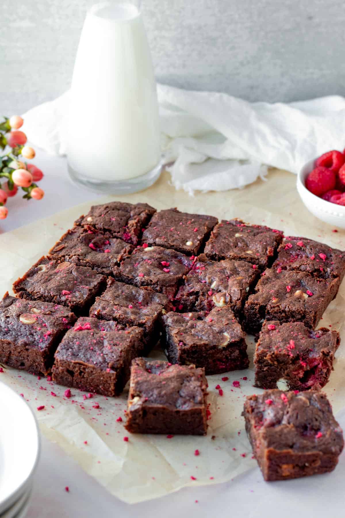 slab of brownies cut into squares with glass of milk and bowl of raspberries in the background