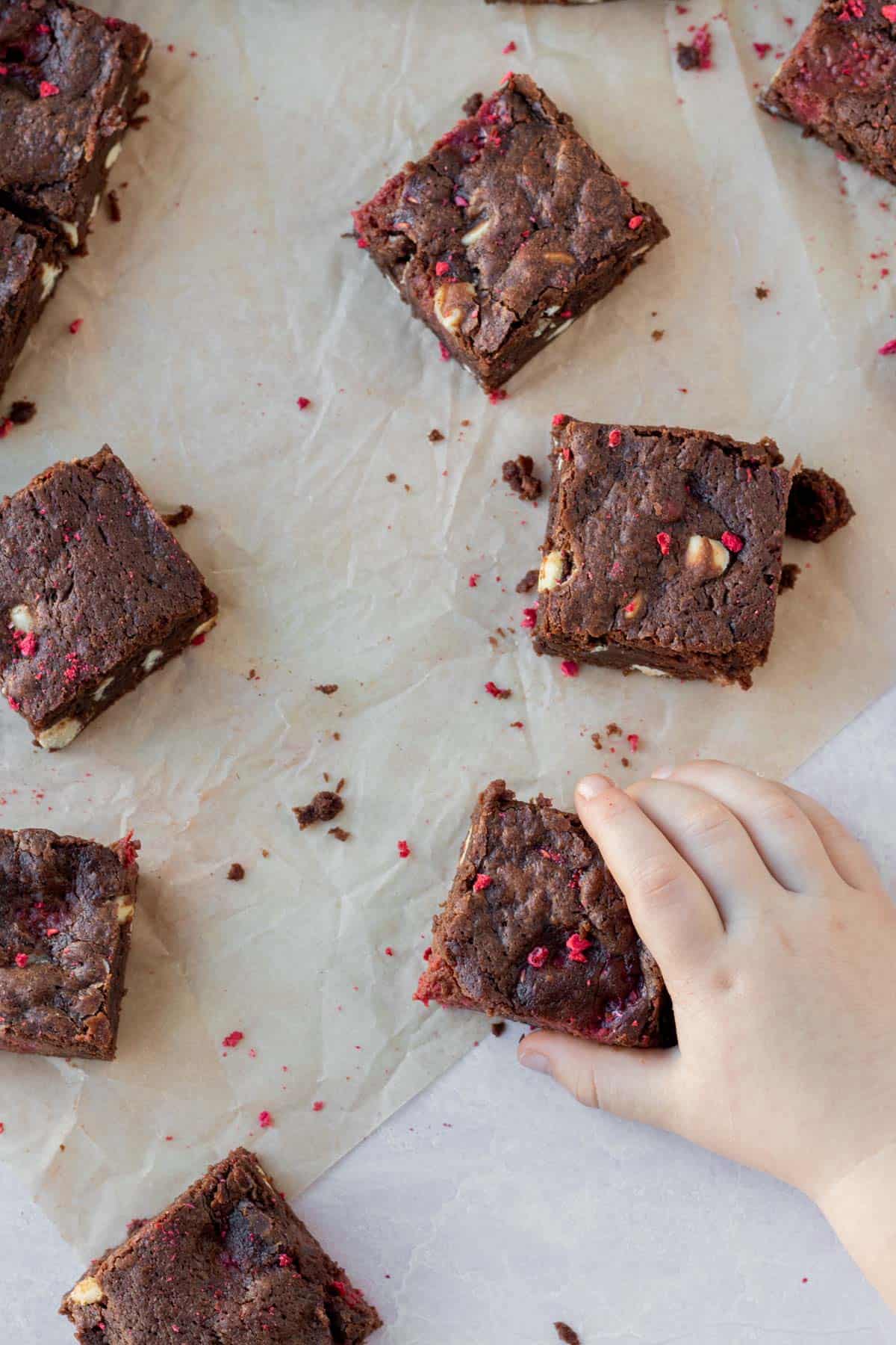 white chocolate and raspberry brownies on a counter with a toddler hand reaching for one