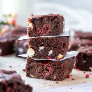 stack of three white chocolate and raspberry brownies with more brownies in the background