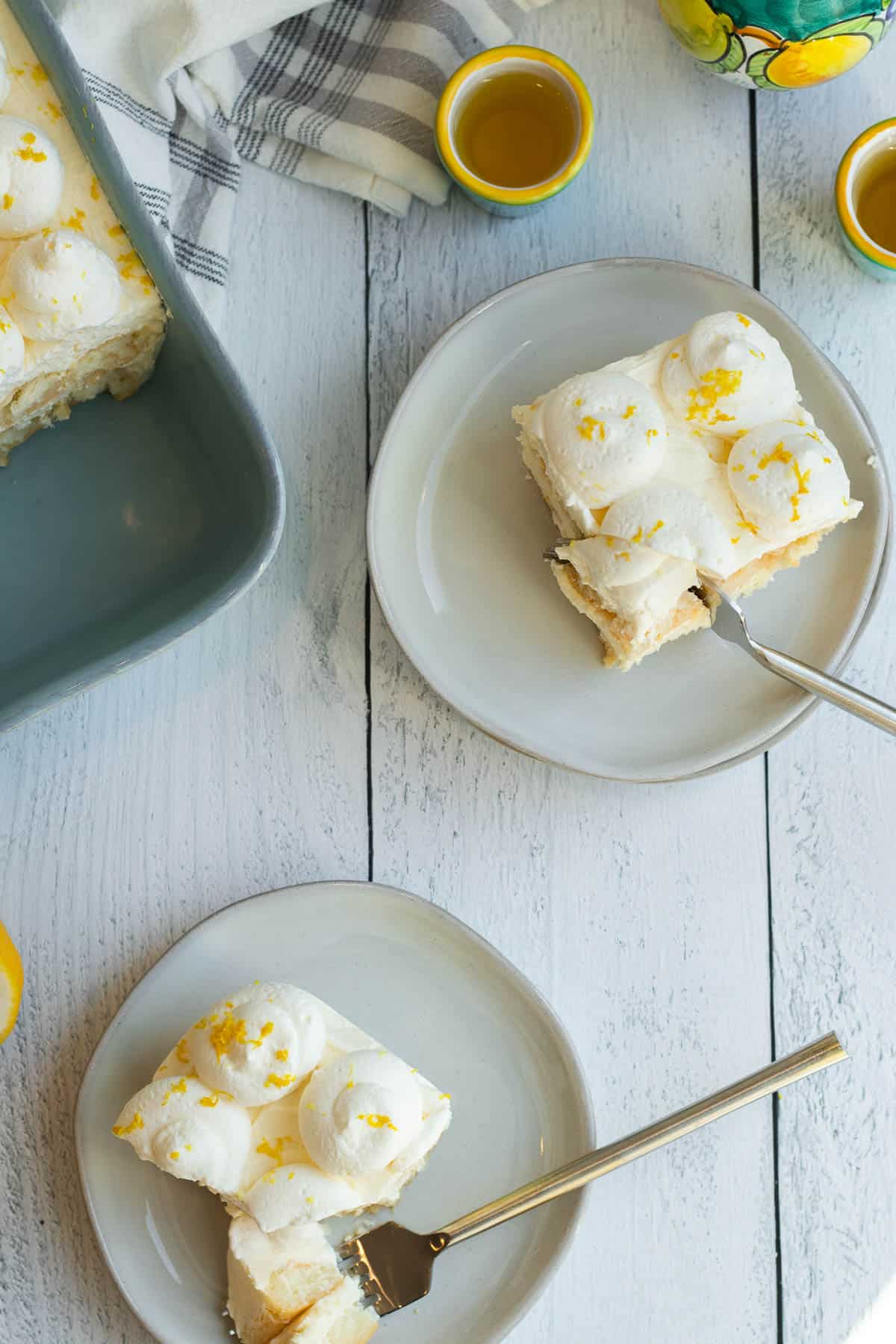 limoncello tiramisu slices on cream colored plates with blue baking dish and cups of limoncello