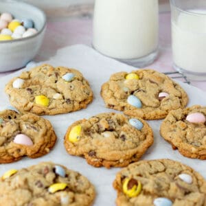 mini egg cookies on parchment paper with glasses of milk in background with bowl of mini egg candies