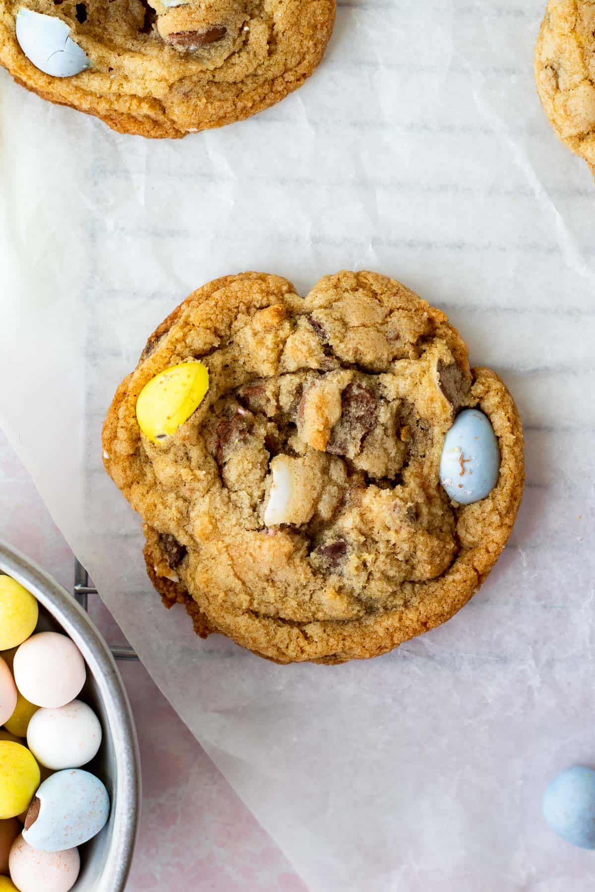 mini egg cookie sitting on cooling rack with parchment on top next to bowl of mini egg candies