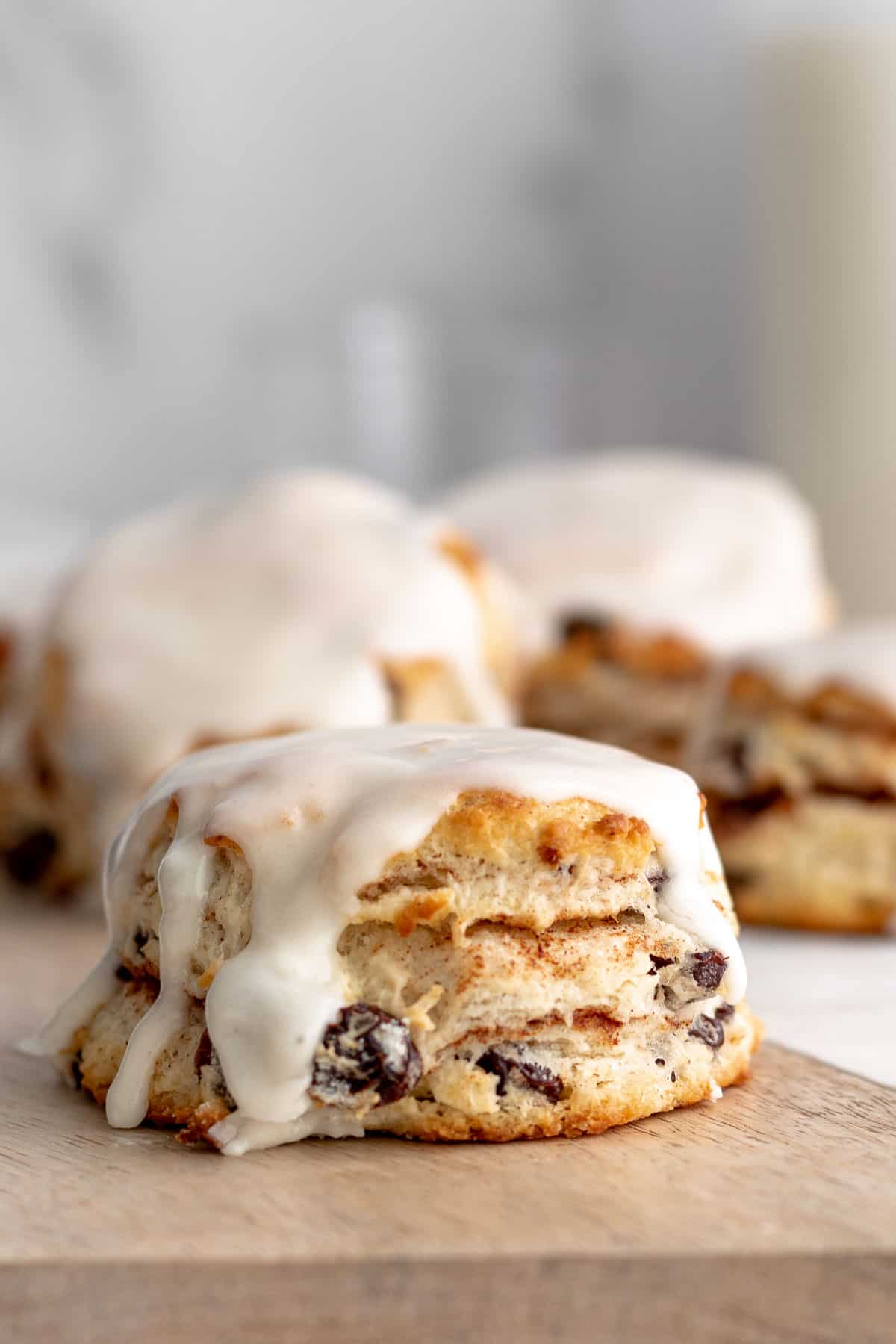 Cinnamon raisin biscuit with a white 
glaze sitting on a wood board with more biscuits in the background