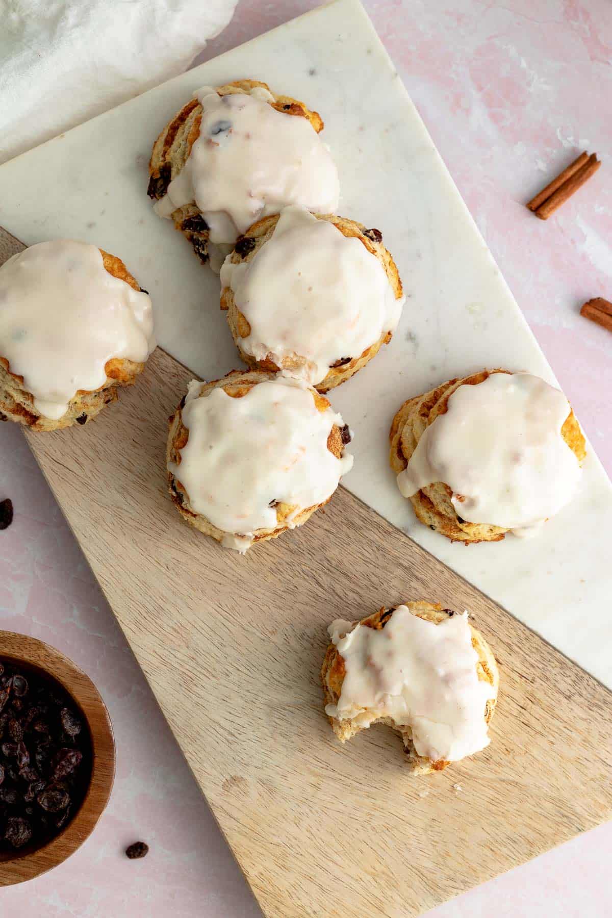 cinnamon raisin biscuits with vanilla glaze sitting on wood and marble cutting board with bowl of raisins next to cutting board