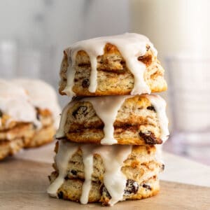 stack of 3 cinnamon raisin biscuits with vanilla glaze dripping down and glass of milk in the background