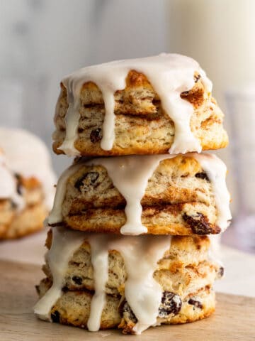 stack of 3 cinnamon raisin biscuits with vanilla glaze dripping down and glass of milk in the background