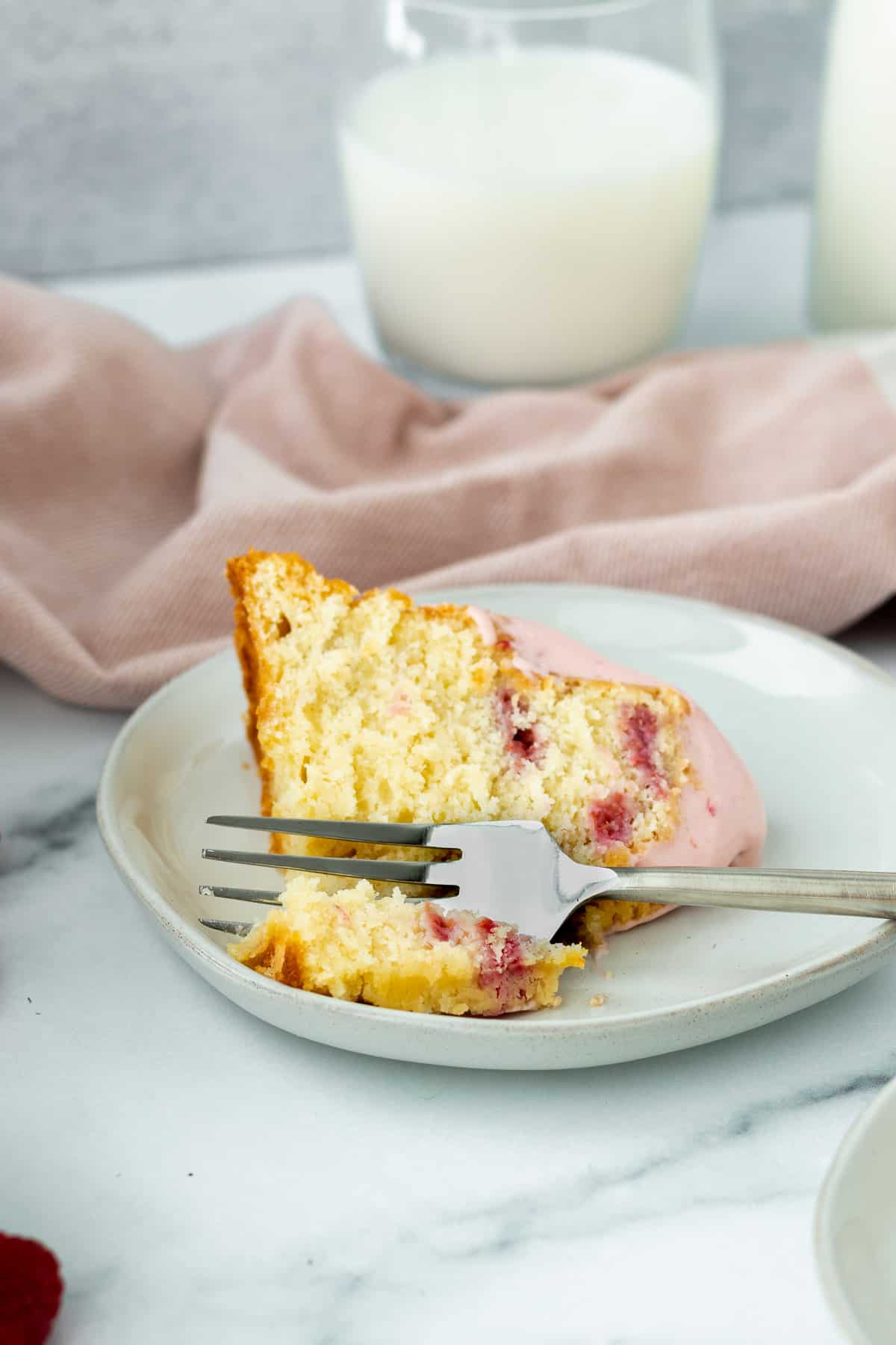 slice of white chocolate raspberry bundt cake on a gray plate with pink linen