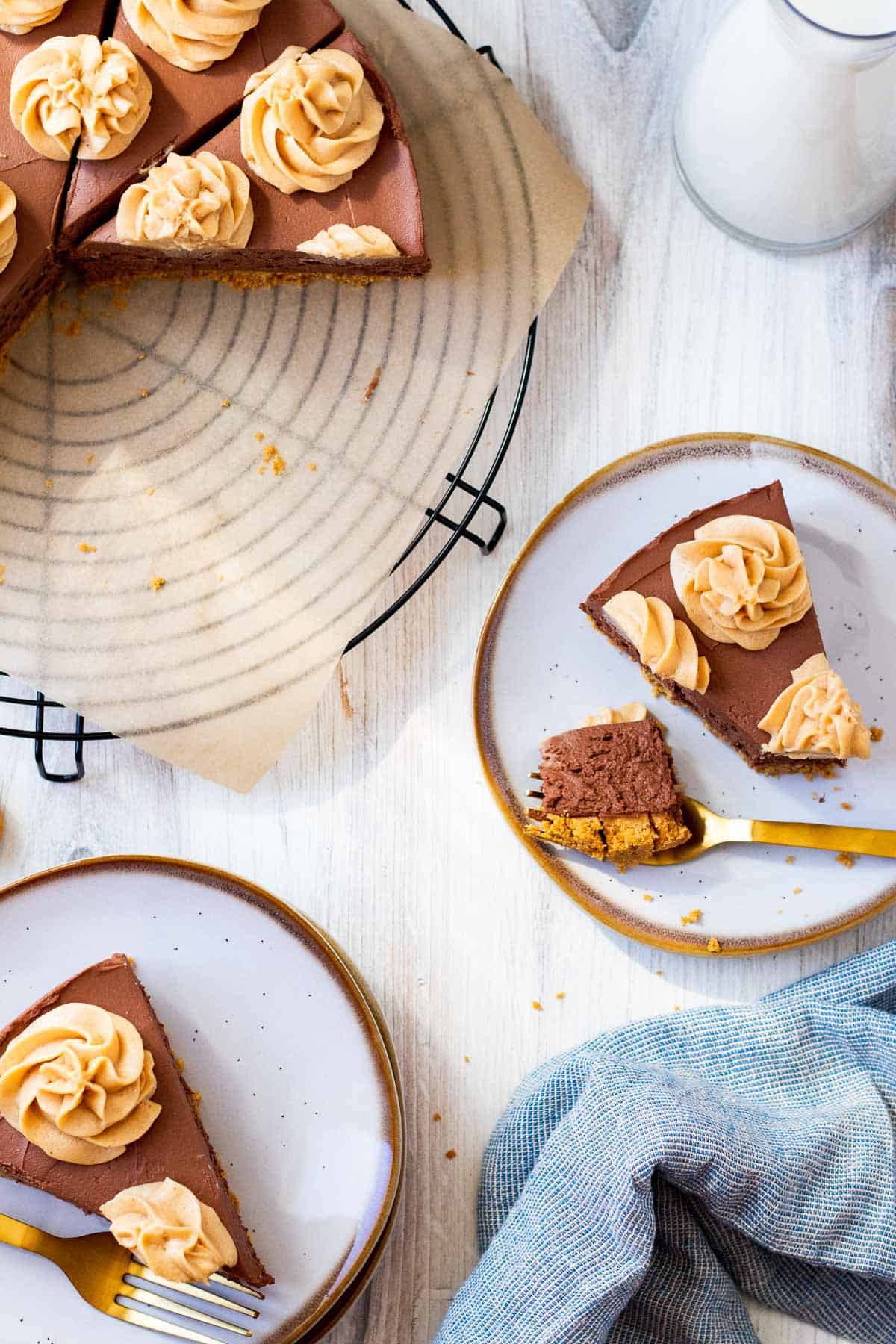 2 white plates with slices of cheesecake and the full cheesecake sitting on a wire rack