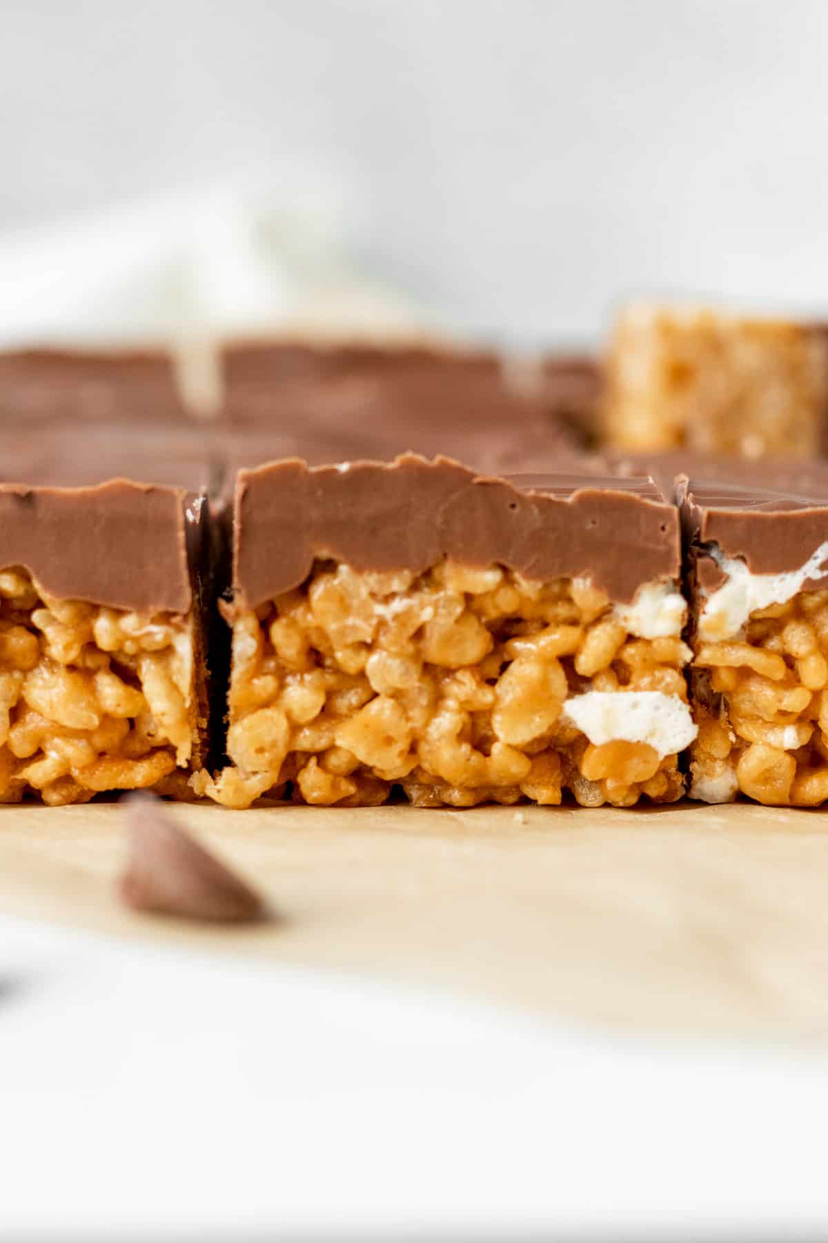 peanut butter rice krispie treats topped with chocolate sitting on brown parchment paper