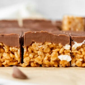 peanut butter rice krispie treats topped with chocolate sitting on brown parchment paper