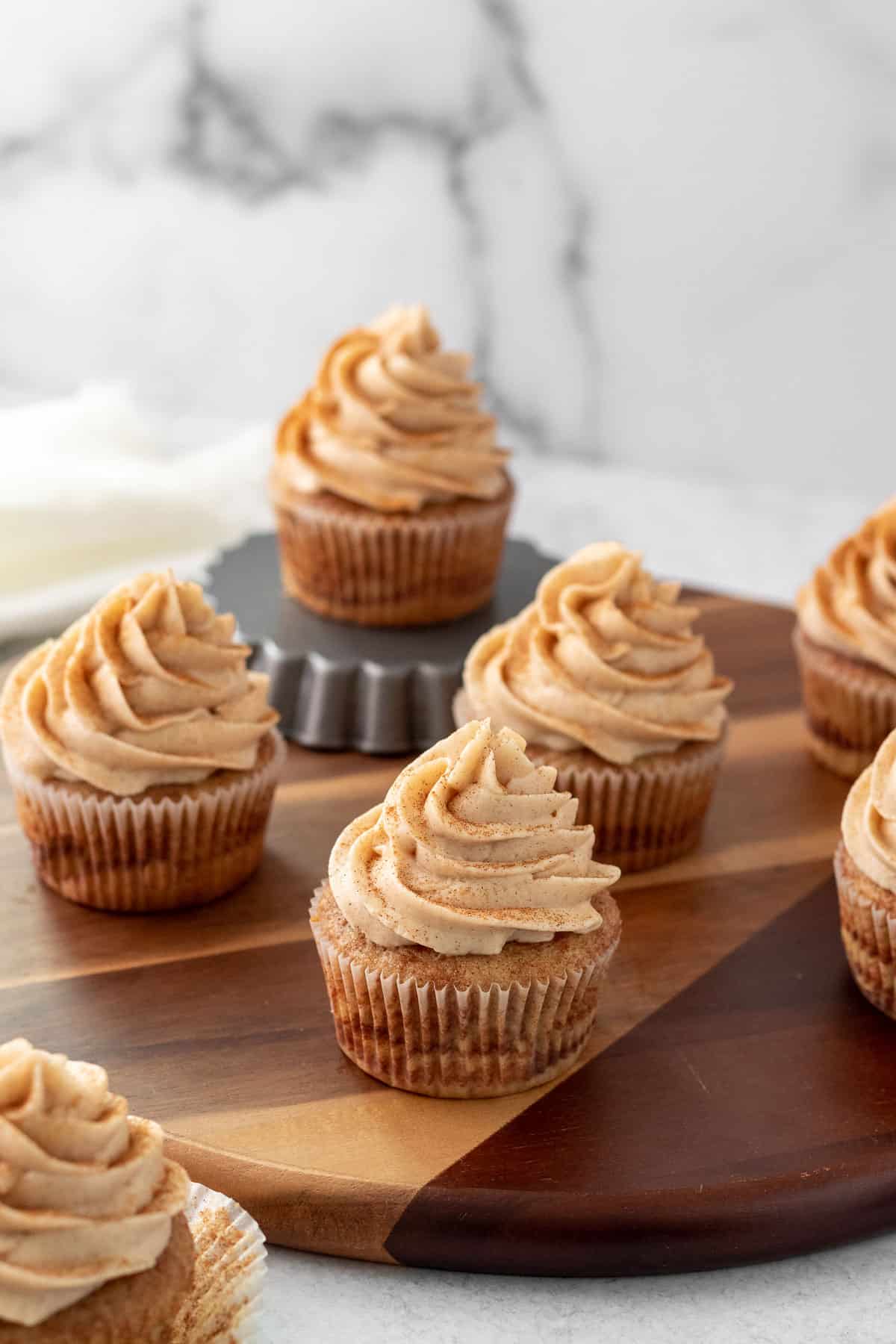 frosted cupcakes sitting on a wood board against a white marble background