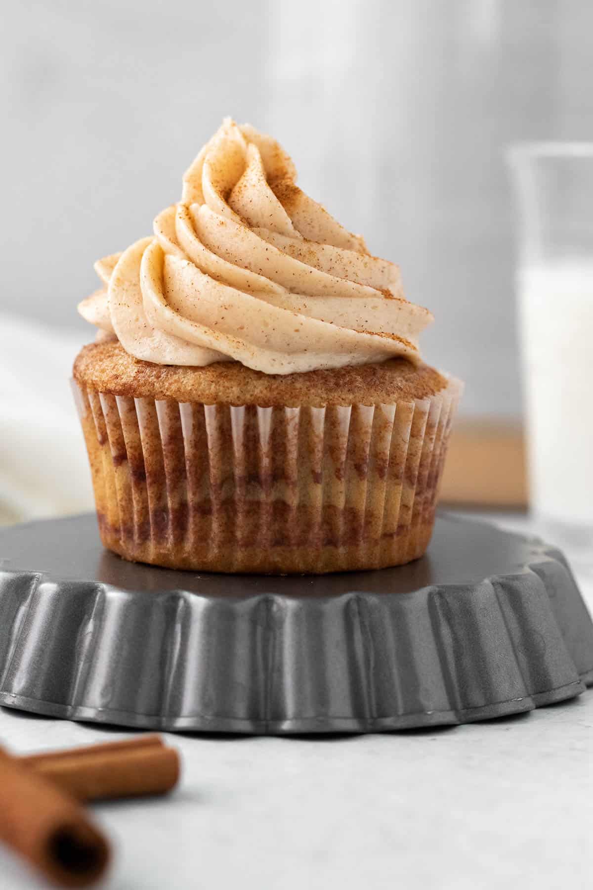 cinnamon cupcake with cinnamon buttercream sitting on an upside down tart pan with a glass of milk in the background