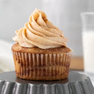 cinnamon cupcake with cinnamon buttercream sitting on an upside down tart pan with a glass of milk in the background