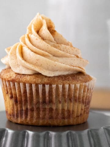 cinnamon cupcake with cinnamon buttercream sitting on an upside down tart pan with a glass of milk in the background