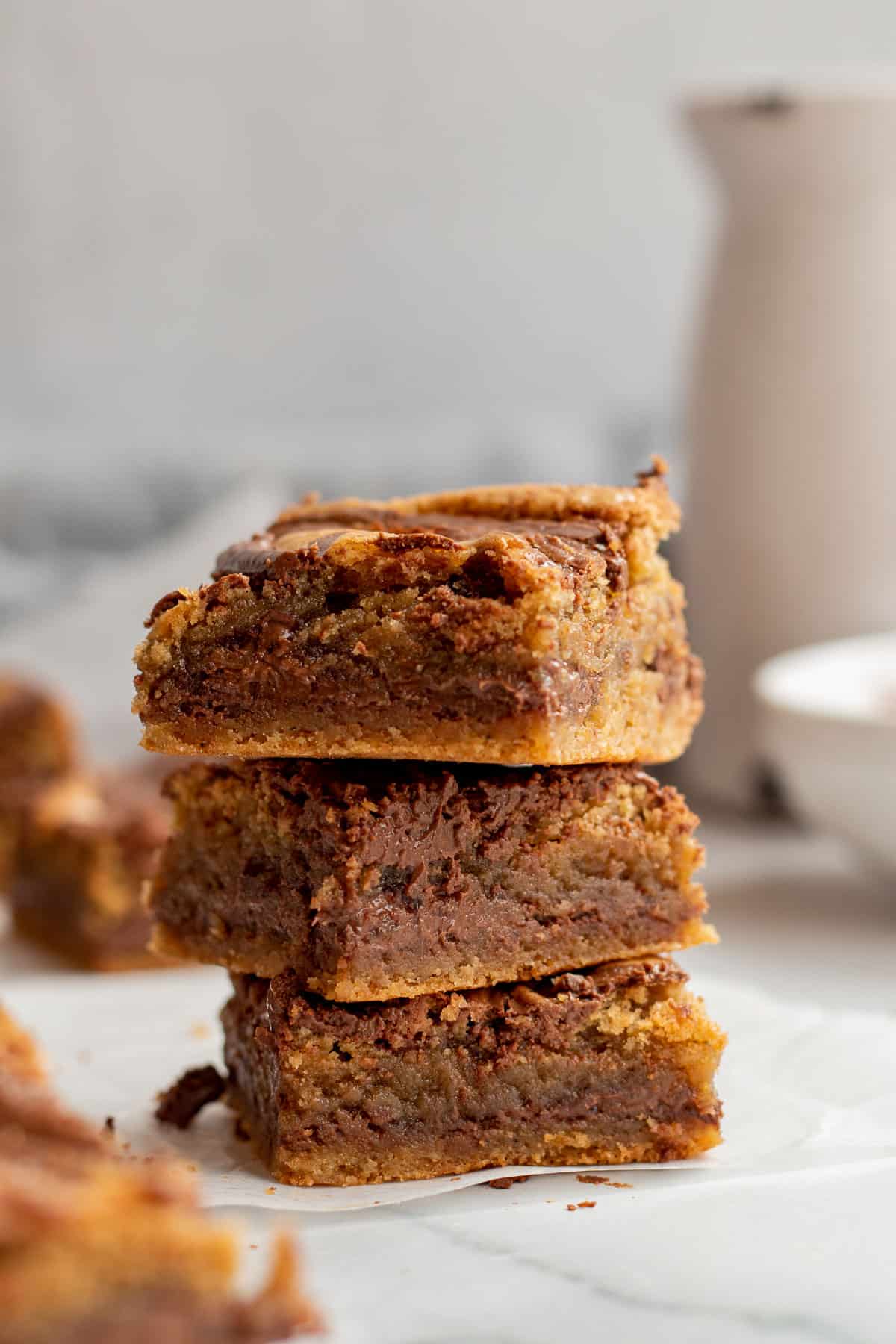 stack of 3 nutella blondies with white bowl and carafe in background