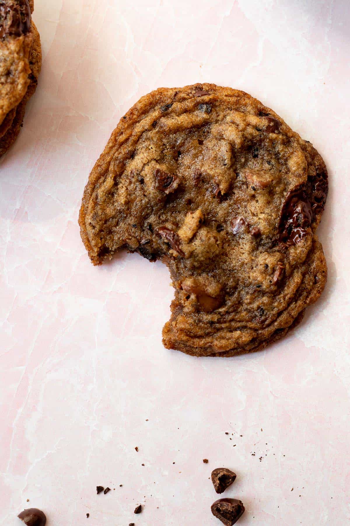 espresso chocolate chip cookie with a bite out of it on a pink background with espresso beans