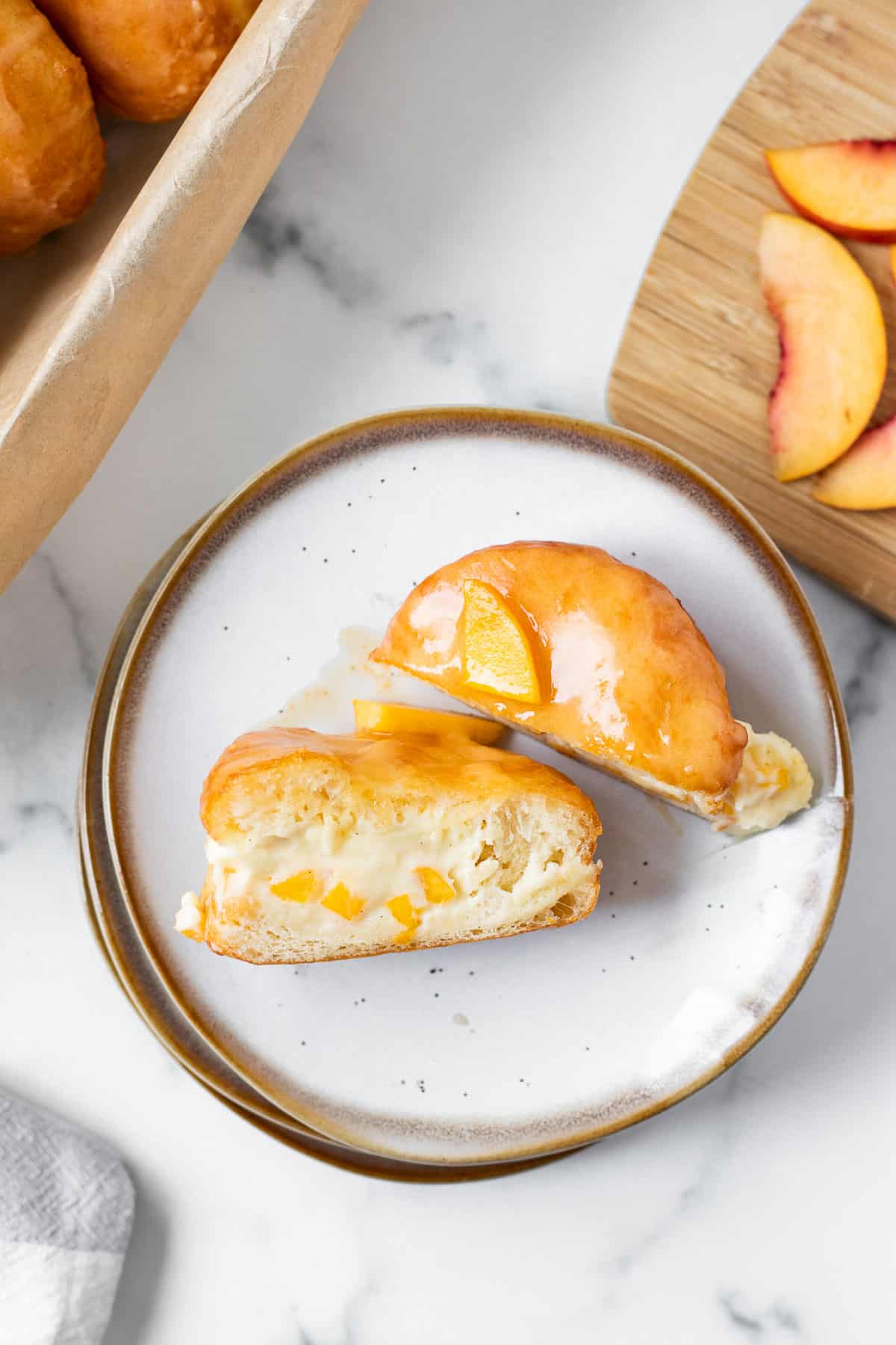 peach donut filled with cream split in half on a stack of plates with cutting board with peaches next to it