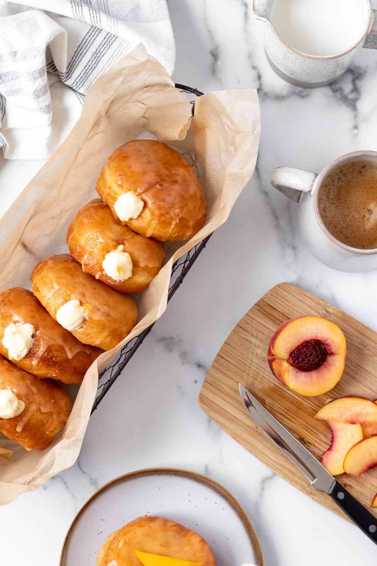 peach doughnuts with vanilla filling in a basket with cutting board with sliced peach