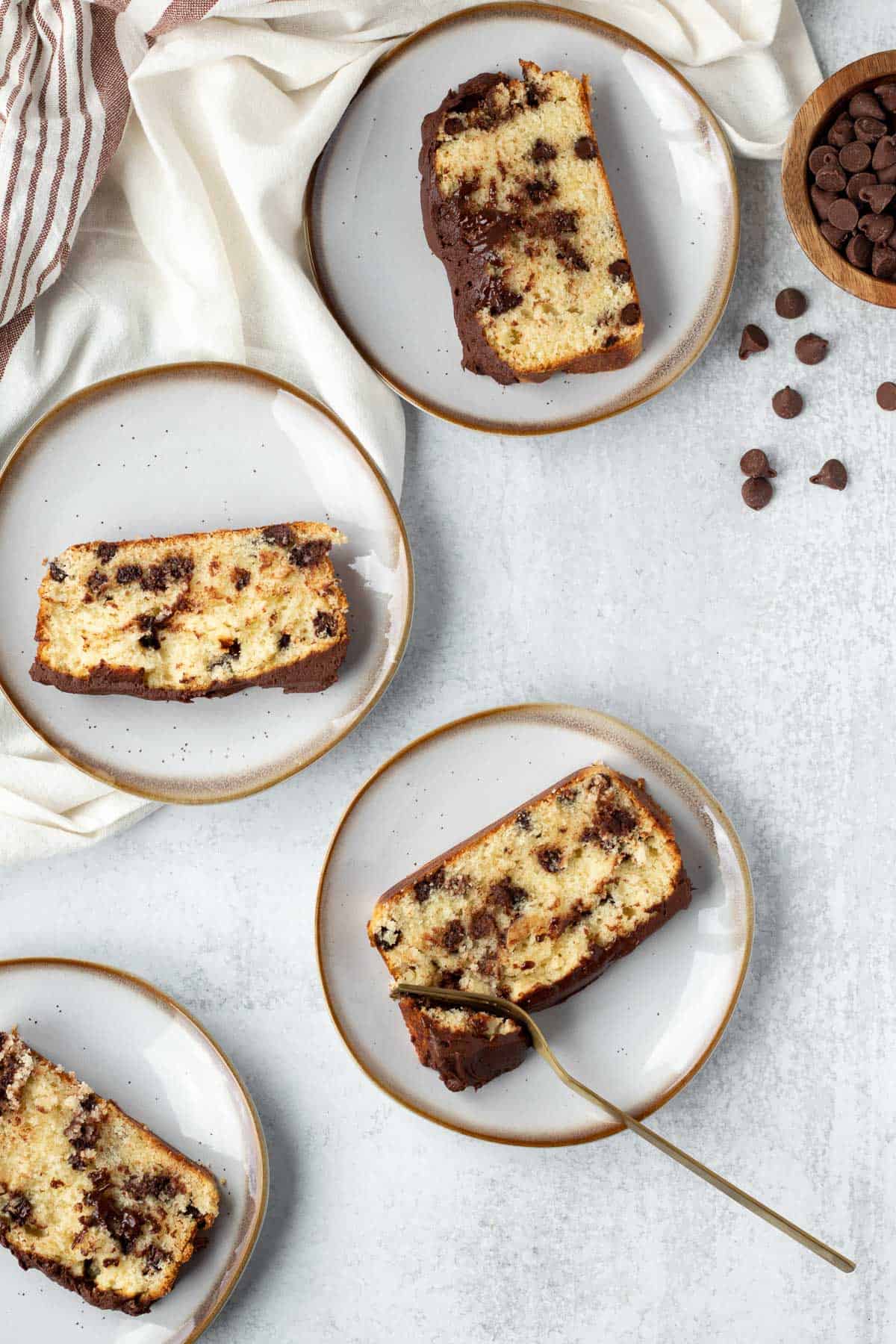 4 plates of chocolate chip loaf cake on gray background with a white linen and chocolate chips