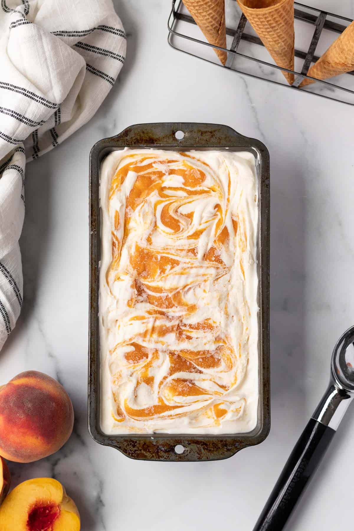 loaf pan filled with peaches and cream ice cream with peach and ice cream scoop on table