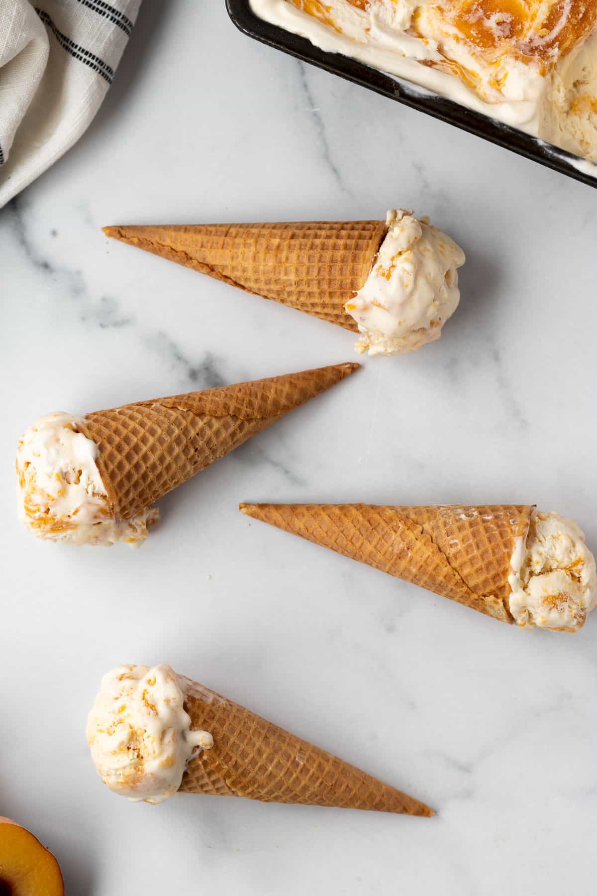 ice cream cones with peaches and cream ice cream laying on a white marble background