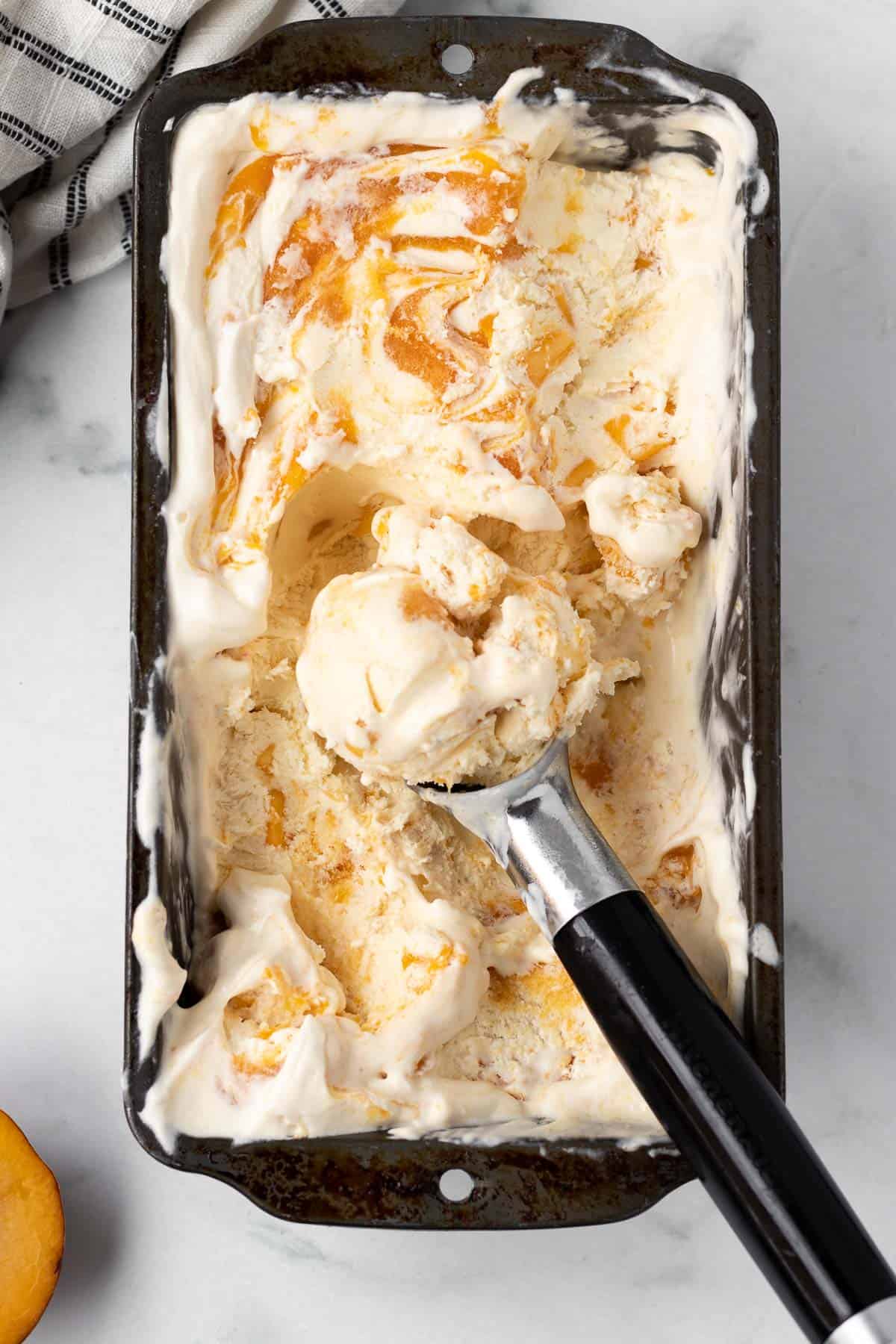 loaf pan with peaches and cream with ice cream scoop of ice cream laying on top.