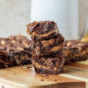 stack of chocolate peanut butter cup brownies on a wood cutting board with a white picture in the background