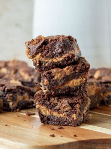 stack of chocolate peanut butter cup brownies on a wood cutting board with a white picture in the background